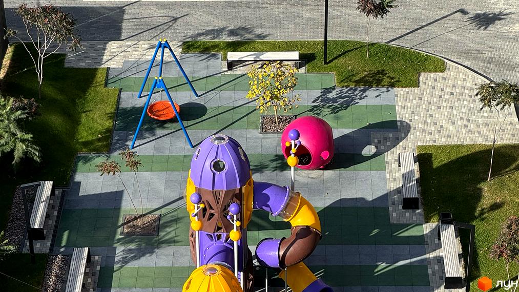 Вид зверху на дитячий майданчик з гірками та гойдалками у Житловому комплексі Стандарт. Облаштована прибудинкова територія з газонами та деревами.