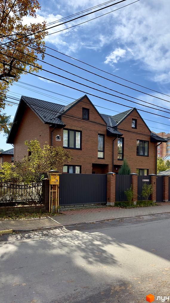 Зображення будинку з червоної цегли у котеджному комплексі PARK PLACE. Перед будинком розташована огорожа та зелені насадження.