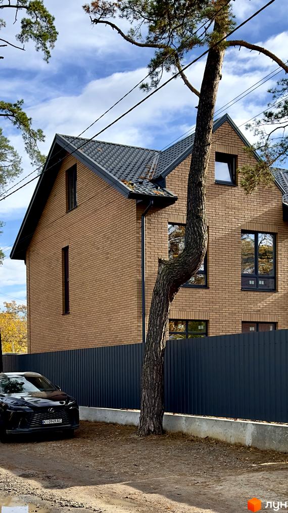 Зображення дуплексу в Житловому комплексі PARK PLACE з цегляним фасадом та темно-сірим дахом. На передньому плані дерево та чорний автомобіль.