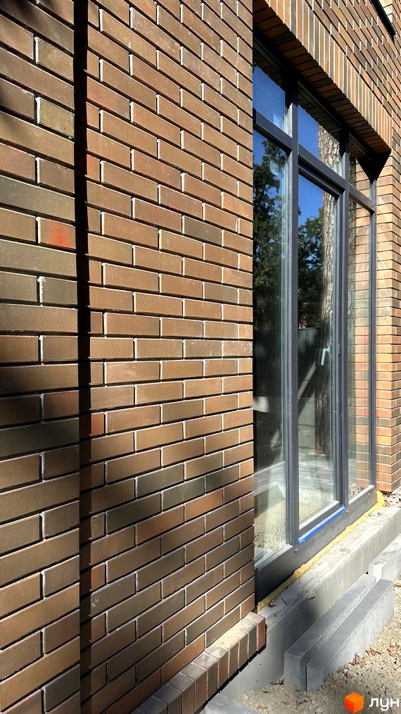 Зовнішній вигляд будинку з вікнами у Котеджному містечку PARK PLACE, збудованого з коричневої цегли. Навколо будинку сіра вимощена територія.