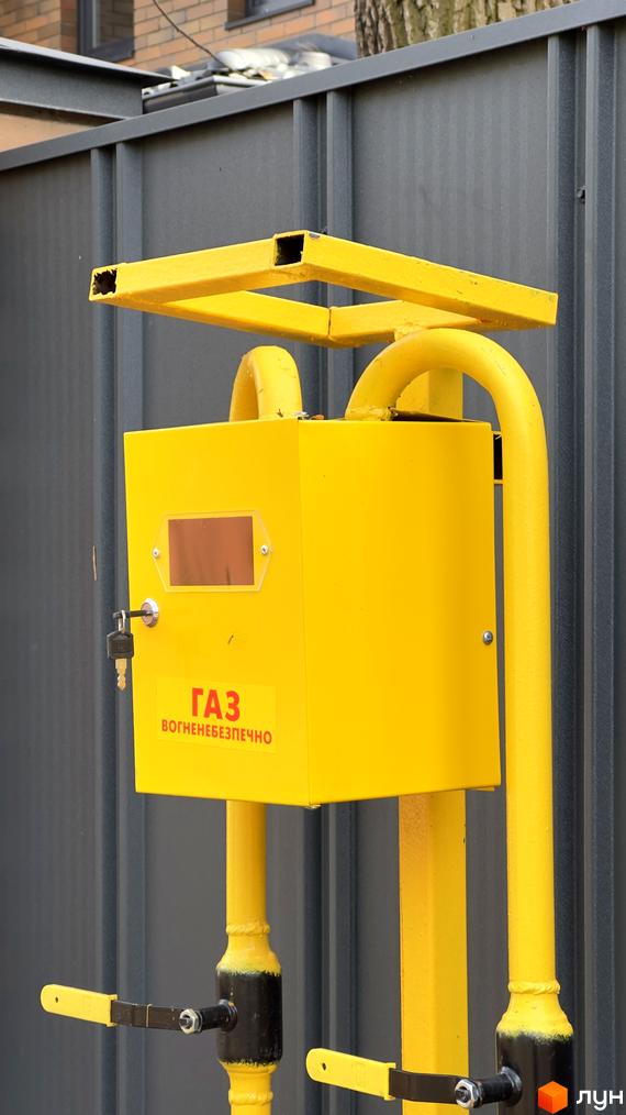 Зовнішній вигляд газового розподільника у Житловому районі PARK PLACE. Жовта конструкція з трубами та запірними кранами біля сірої стіни.