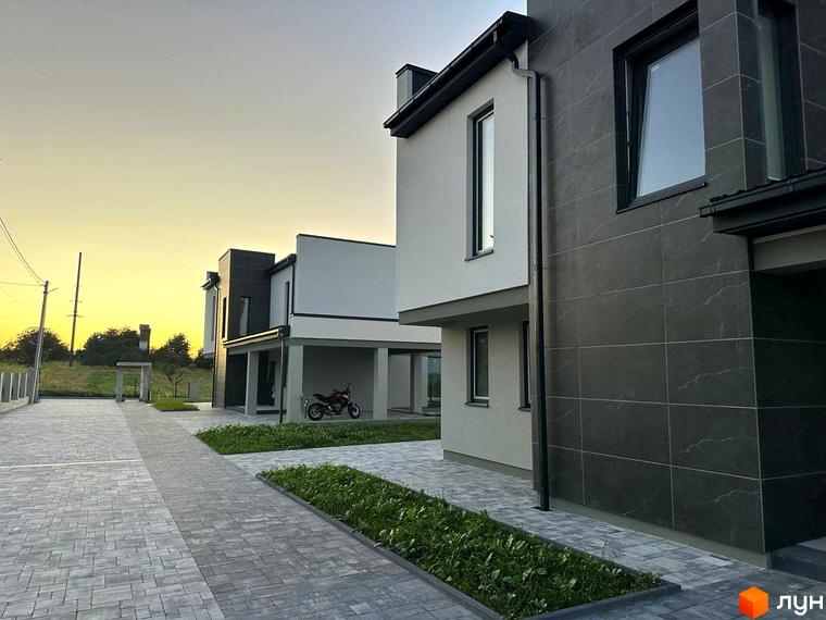 Зображення будинку в Котеджному містечку Belvedere. Вигляд фасаду будинку з великими вікнами та прибудинковою територією.