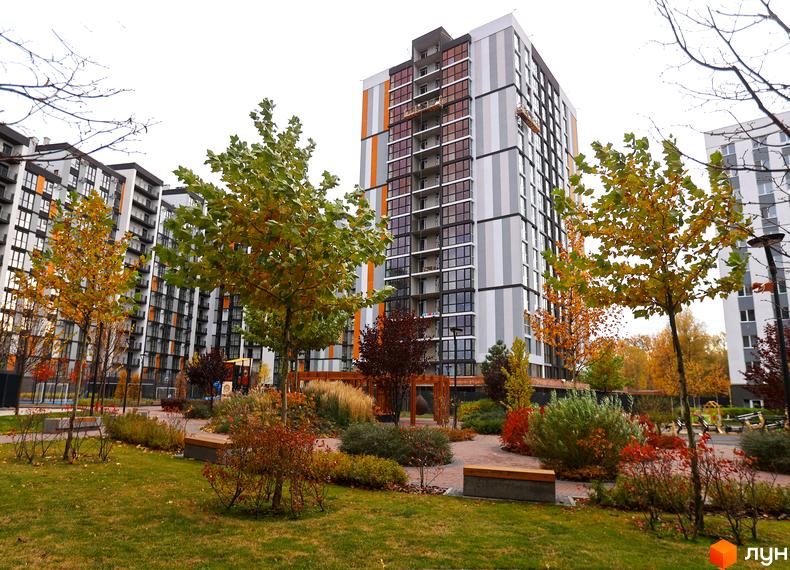 Висотна будівля ЖК Атмосфера з панорамними вікнами та яскравими фасадами. На території комплексу облаштовані зелені зони з деревами та лавками.