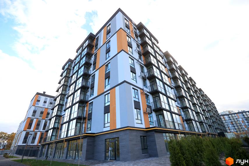 Багатоповерховий будинок ЖК ATMOSFERA LIFE з панорамними вікнами та балконами. На прибудинковій території зелені насадження та доріжки.