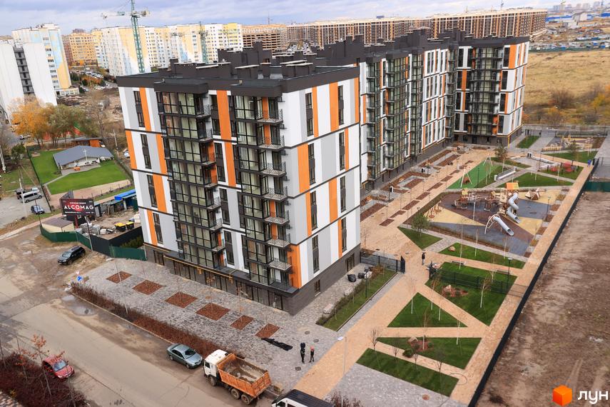 Високоповерховий будинок ЖК ATMOSFERA LIFE з фасадом в сірих, білих та помаранчевих кольорах. На прибудинковій території дитячий майданчик та зони відпочинку.