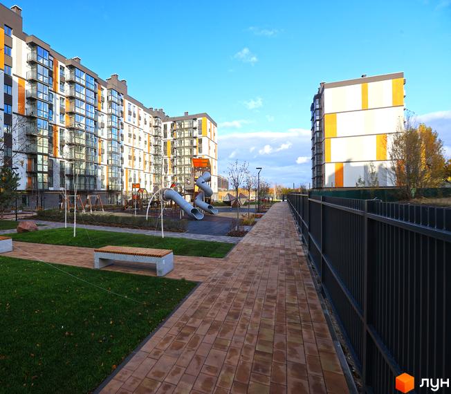 Житловий комплекс ATMOSFERA LIFE з фасадами в світлих тонах та дитячим майданчиком на території. Благоустрій прибудинкової території.