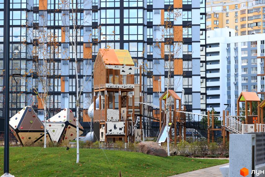 Житловий комплекс ATMOSFERA LIFE з дитячим майданчиком на тлі багатоповерхового будинку з великими вікнами.