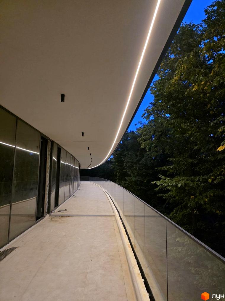 Житловий комплекс Emily Apartments з виходом на терасу, скляною огорожею та освітленням. Навколо зелені дерева.