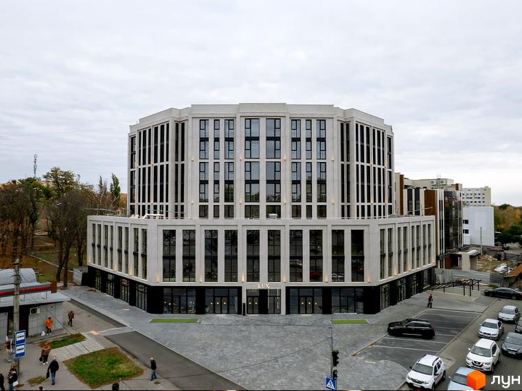 Житловий комплекс Standard LUX з багатоповерховими будівлями та паркінгом. Зовнішній вигляд новобудови з фасадами з білої цегли та великими вікнами. Прибудинкова територія з бруківкою та зеленими зонами.