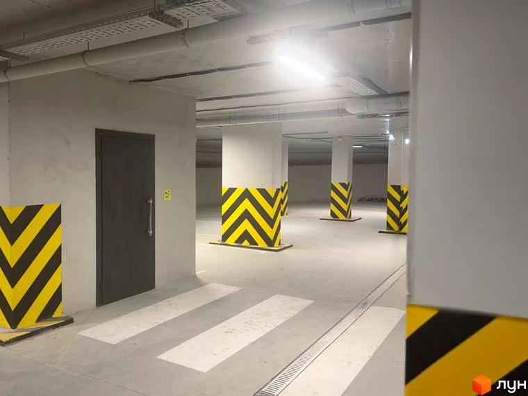 Підземний паркінг у житловому комплексі Standard LUX з розміткою та захисними елементами на колонах. Внутрішній простір паркінгу з дверима та пішохідним переходом.