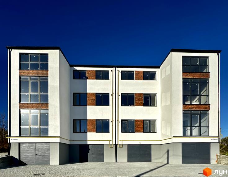 Новобудова ЖК Затишок з цегляними вставками та великими вікнами на тлі ясного неба. Перед будинком розташований бруківковий двір та гаражні ворота.