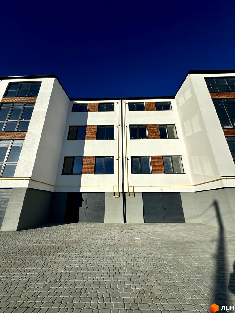 Зовнішній вигляд новобудови ЖК Затишок з цегляними та білими фасадами, великими вікнами та бруківкою на прибудинковій території.