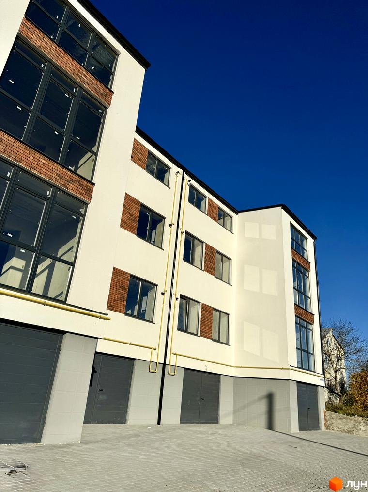 Зовнішній вигляд новобудови ЖК Затишок з цегляними вставками та великими вікнами. Прибудинкова територія з гаражними воротами та бруківкою.