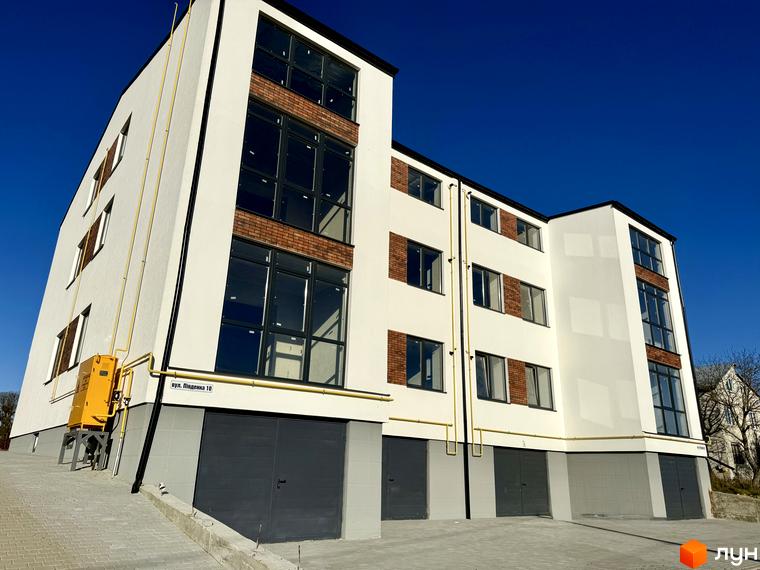 Зовнішній вигляд новобудови ЖК Затишок з цегляними вставками та великими вікнами, перед будинком розташована прибудинкова територія з під'їзними шляхами.