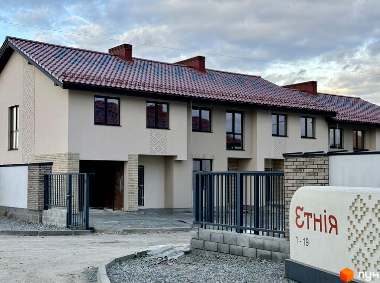 Котеджне містечко Етнія: фасади двоповерхових будинків з червоною черепицею та цегляними елементами, перед ними - ворота та вивіска з назвою комплексу.
