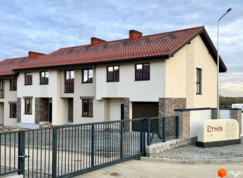 Котеджне містечко КМ Етнія: фасади будинків з червоною черепицею та цегляними елементами, огороджена територія з кованими воротами.