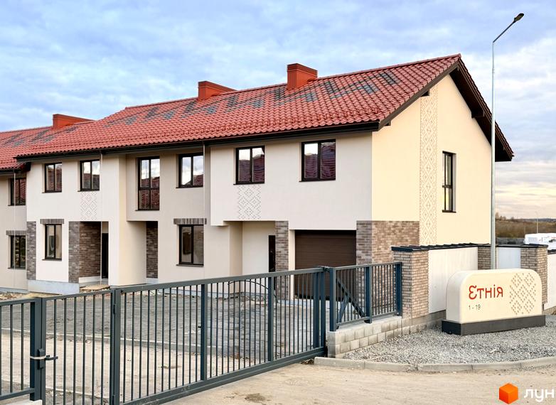 Котеджне містечко Етнія: фасади будинків з червоною черепицею та цегляними елементами, огороджена територія з воротами та інформаційним стендом.