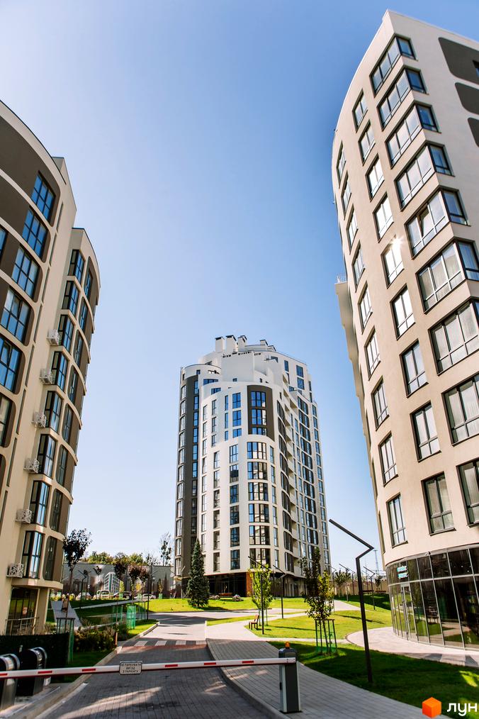 Новобудова Парус City з вигнутими фасадами та панорамними вікнами на тлі блакитного неба. На прибудинковій території доглянутий газон та дерева.