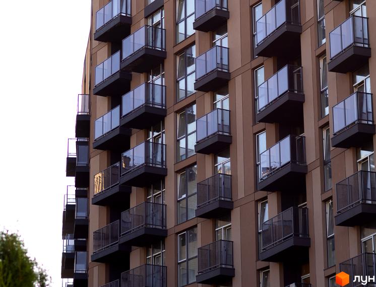 Зовнішній вигляд новобудови Pokrovsky Apart Complex з балконами та вікнами. Фасад будівлі коричневого кольору.