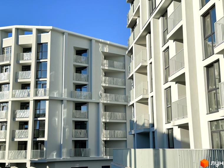 Зовнішній вигляд житлового комплексу Pokrovsky Apart Complex з балконами та вікнами на тлі блакитного неба. Навколо будівлі розташована прибудинкова територія.