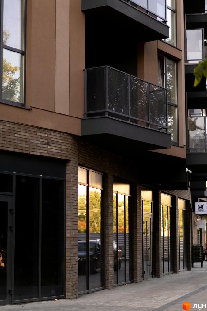 Зовнішній вигляд будинку Pokrovsky Apart Complex з цегляним та коричневим фасадом, великими вікнами та балконами. Поруч розташована бруківка та дерева.