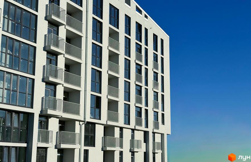 Фасад житлового комплексу Pokrovsky Apart Complex з численними балконами та великими вікнами на фоні блакитного неба. Новобудова має сучасний дизайн.