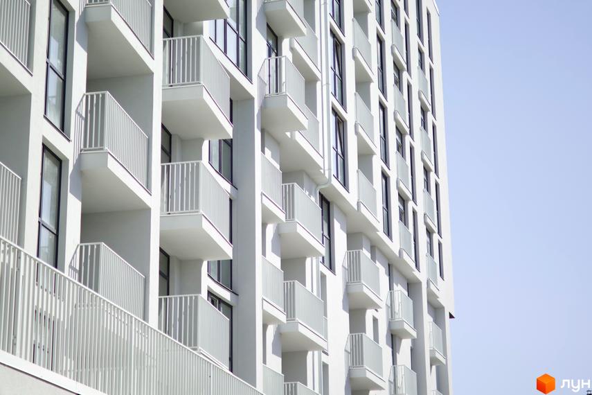 Pokrovsky Apart Complex - новобудова з численними балконами та вікнами на тлі блакитного неба. Фасад будівлі виконаний у білому кольорі.