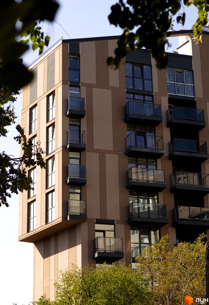 Зовнішній вигляд будинку Pokrovsky Apart Complex з балконами та вікнами, оточений деревами. Новобудова з коричневим фасадом.