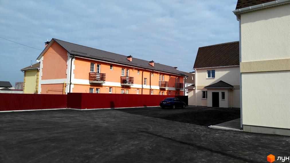 Житловий комплекс з помаранчевими будинками з балконами та темно-коричневим дахом. На території комплексу є парковка та червоний паркан.