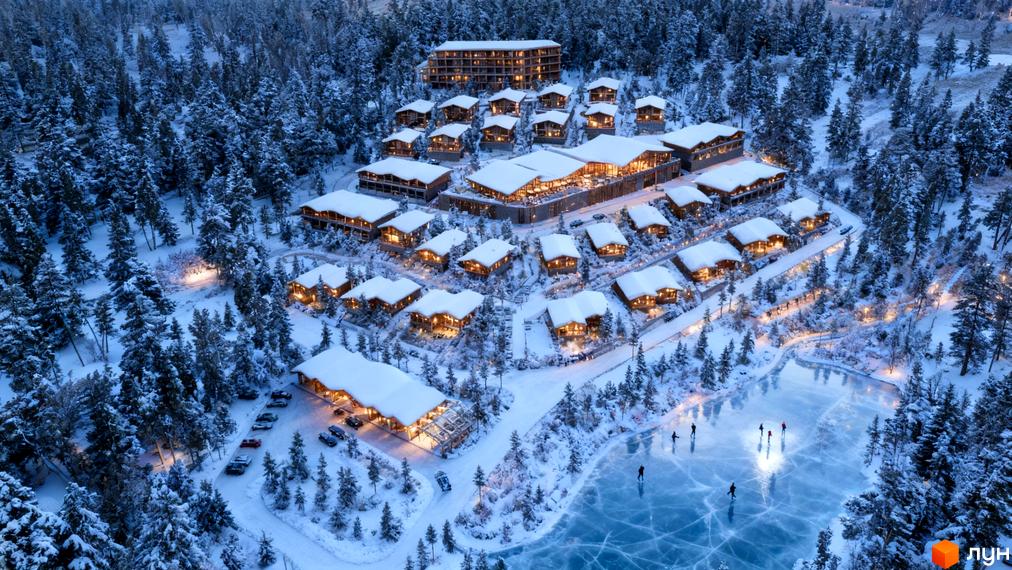 Котеджне містечко Chamonix Premier Resort взимку, з дерев'яними будинками під снігом та замерзлим озером, де катаються люди.