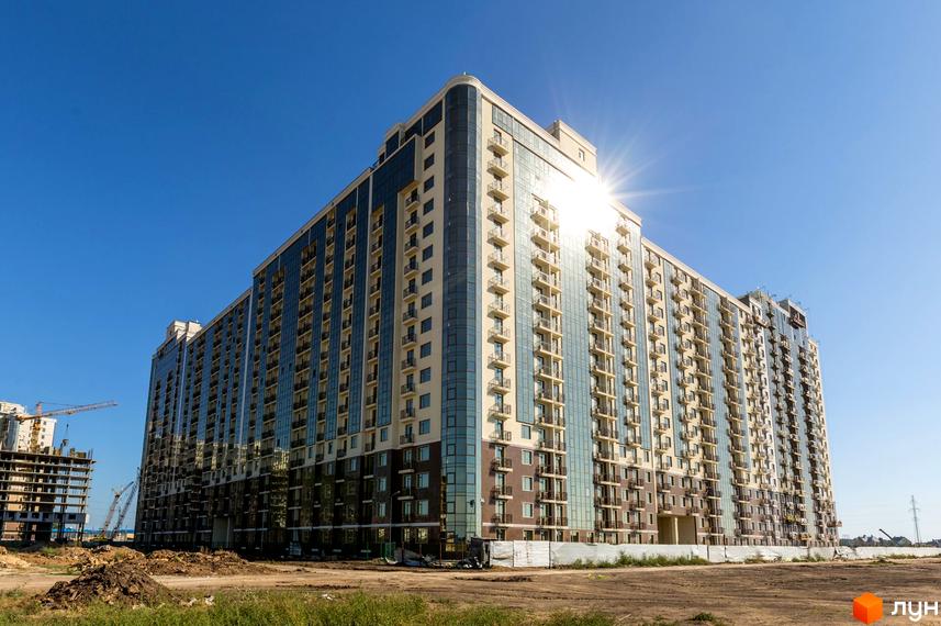 Житловий комплекс Пятая Жемчужина з сучасним фасадом та балконами. Прибудинкова територія з будівельними роботами та зеленою зоною.