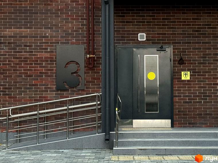 Вхідна група новобудови ЖК Стандарт з пандусом та сходами, облицьована цеглою. Зовнішній вигляд будівлі та прибудинкової території.