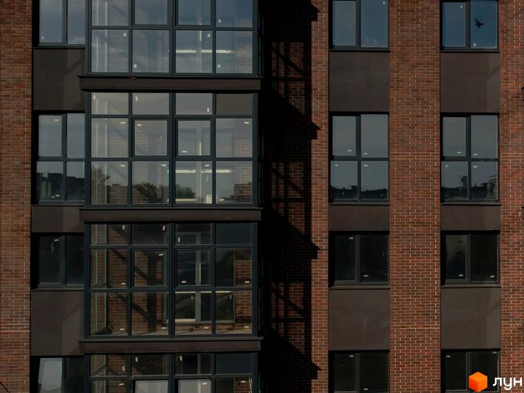 Фасад житлового комплексу Стандарт з цегляним оздобленням та великими вікнами. Вікна виходять на прибудинкову територію.