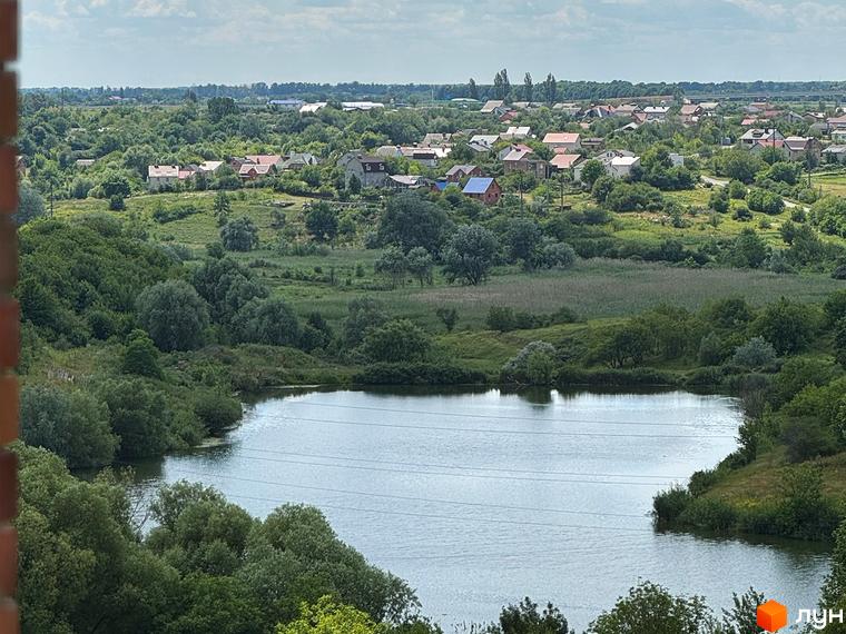 Вид на житловий комплекс Стандарт з мальовничим озером та зеленою територією. Будинки розташовані серед дерев та полів.