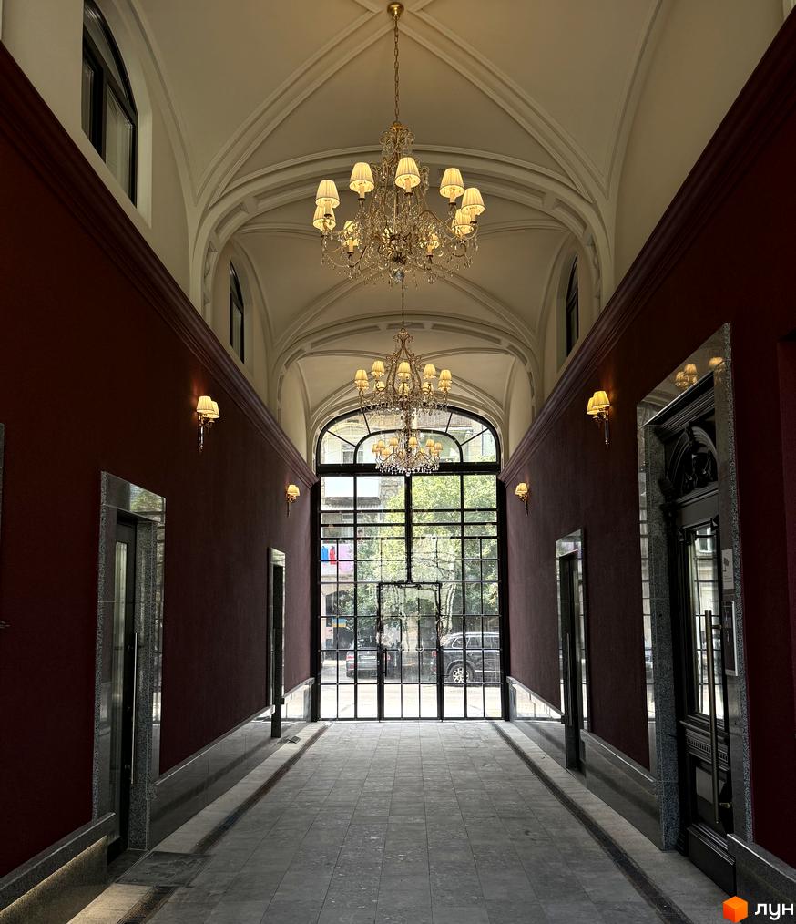 Житловий комплекс Гімназист: розкішний хол з кришталевими люстрами та великим вікном, що виходить на зелену зону.