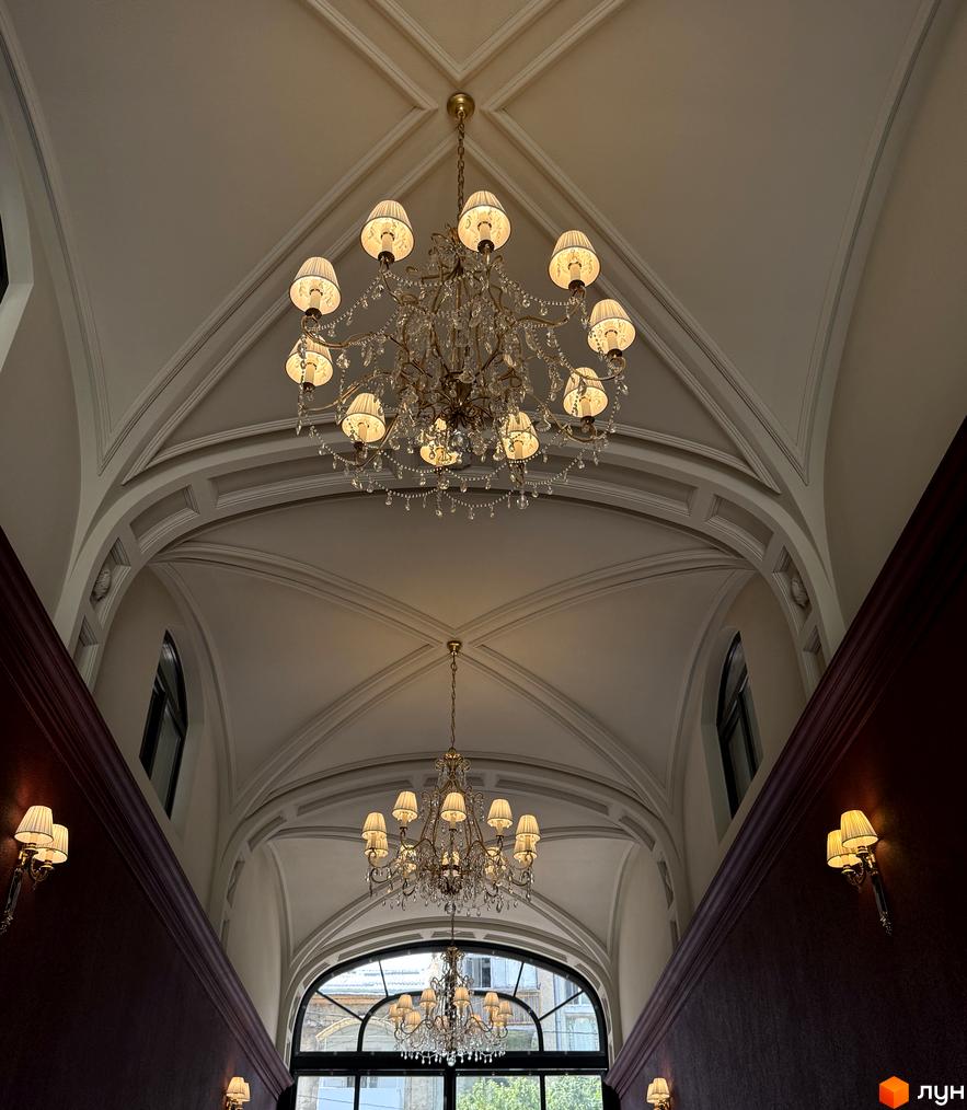 Розкішні люстри та стінові світильники в інтер'єрі житлового комплексу Гімназист. Високі стелі з архітектурними елементами.