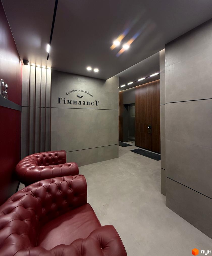 Житловий комплекс Гімназист: сучасна новобудова з червоними диванами та дерев'яними елементами біля ліфта.
