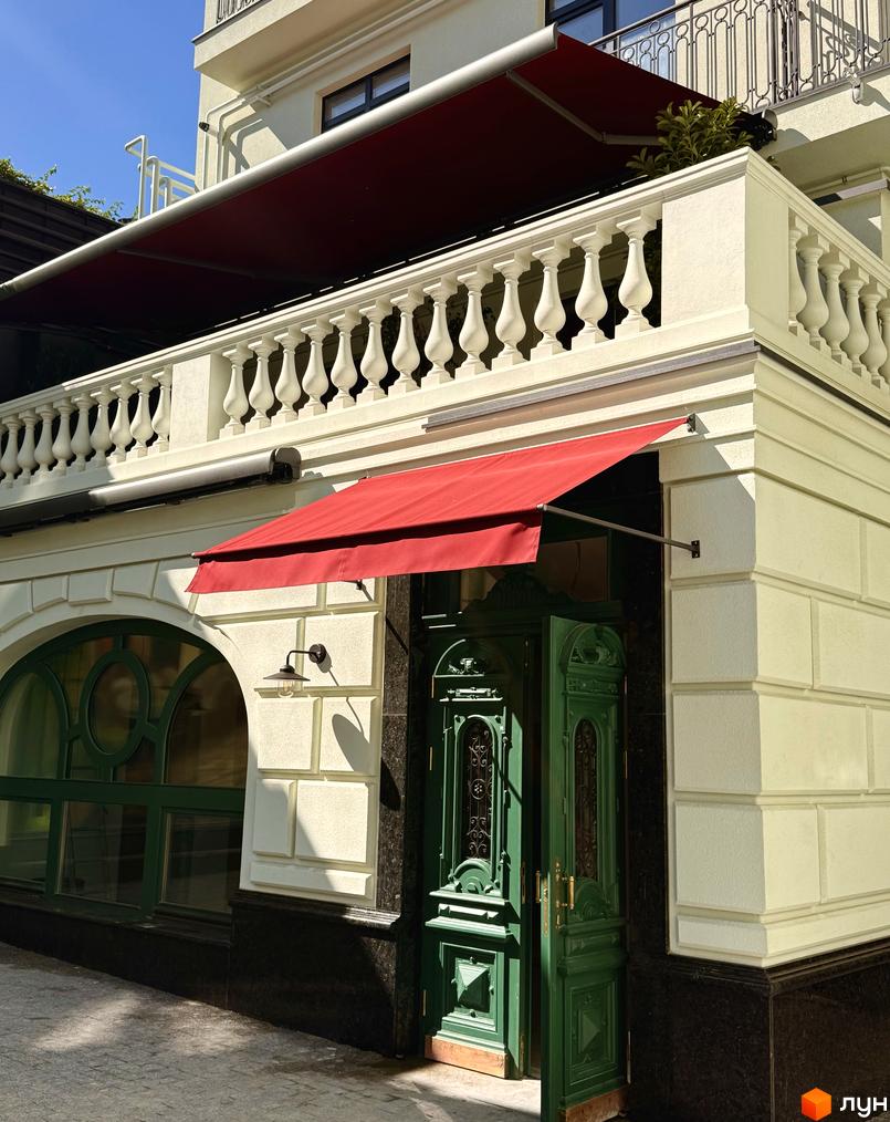 Житловий комплекс Гімназист: фасад будівлі з червоним навісом над входом та білими балюстрадами. Зелені вікна та двері додають елегантності.