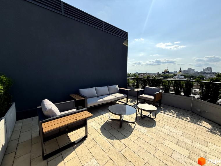 Житловий комплекс Гімназист: тераса з диваном та кріслами на тлі міського пейзажу. Сучасна зона відпочинку на даху новобудови.