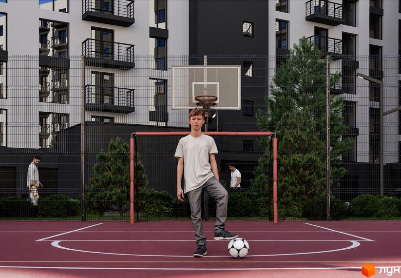 Житловий комплекс Урожайний: фасади будівель та спортивний майданчик з баскетбольним кільцем та футбольними воротами. Хлопець стоїть на полі з м'ячем.
