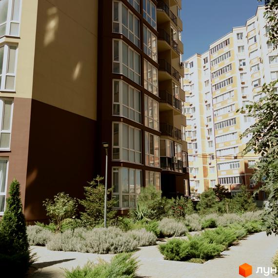 Житловий комплекс Нова Європа. Фасад будинку з коричневими та бежевими елементами, великими вікнами та балконами. Навколо доглянута прибудинкова територія з кущами та деревами.