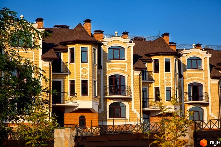 Житловий комплекс з жовтої цегли з коричневим дахом. На території комплексу є дерева та кований паркан.