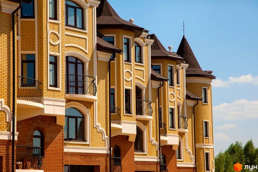 Зовнішній вигляд будинку житлового комплексу КМ Хутір Ясний. Житловий комплекс з жовтої цегли з балконами та вікнами.