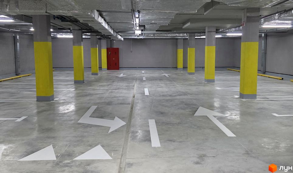 Підземний паркінг ЖК Eco Dream з жовтими колонами та розміткою напрямків руху. Бетонна підлога та сірі стіни створюють функціональний простір.