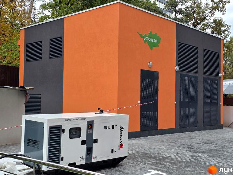 Будівельний проєкт Eco Dream з оранжево-сірим фасадом та дизельним генератором на бруківці.