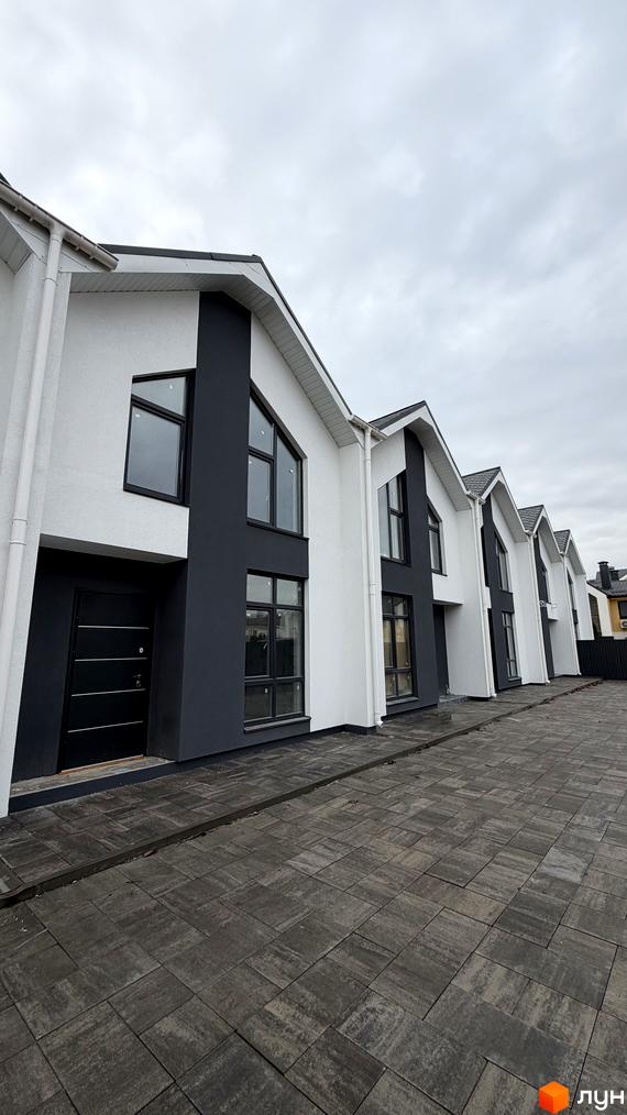 Білосніжні таунхауси з темними акцентами та великими вікнами у житловому комплексі. Бруківка на прибудинковій території.