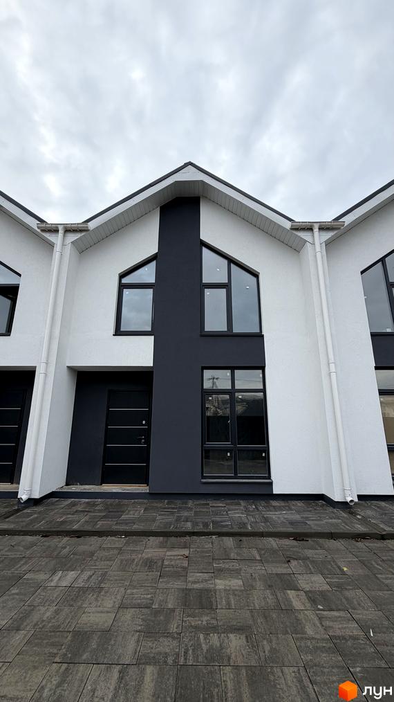 Фасад таунхаусу в ЖК Комфортний квартал DeLuxe з білими стінами, чорними вікнами та вхідними дверима, бруківка на прибудинковій території.