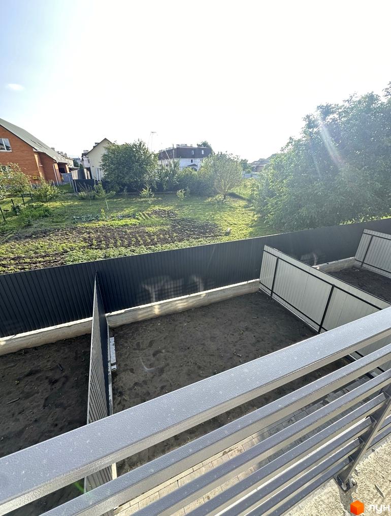 Вид на таунхауси ЖК Комфортний квартал DeLuxe. Огороджена прибудинкова територія з газоном та парканом, поруч зелені насадження та будинки.