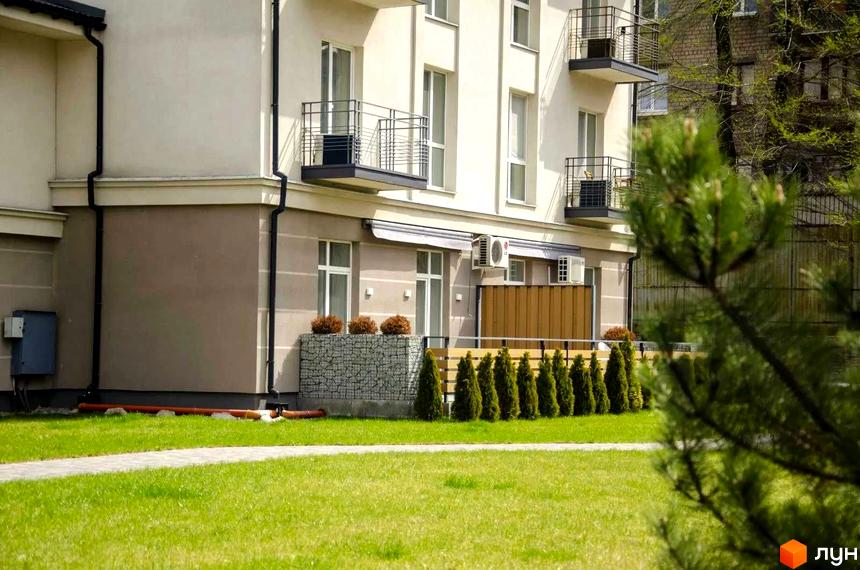 Зображення будинку житлового комплексу Затишна Оселя з балконами, поруч газон та декоративні рослини.