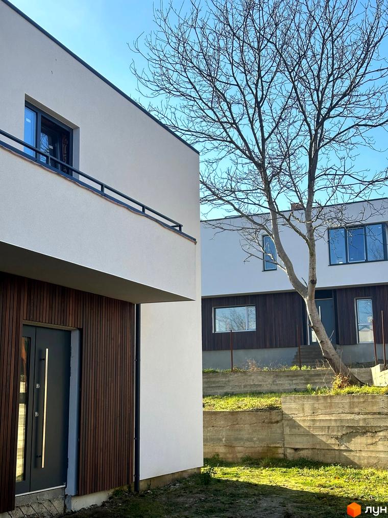 Фасад будинку в Котеджному містечку Hillside з панорамними вікнами та дерев'яним оздобленням. На прибудинковій території газон та дерева.